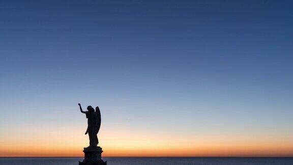 从夜晚到白天一个天使雕像与日出在海洋上的时间流逝