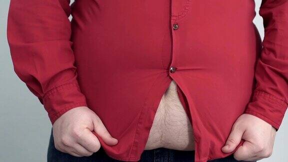 一个胖乎乎的男人试图在他的大肚子上拉衬衫纽扣被扯掉了慢动作