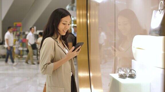 年轻的亚洲妇女走着看着服装店的橱窗
