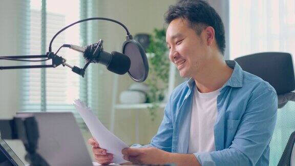 亚洲迷人的音频DJ男子对着麦克风对广播讲话年轻英俊的博主男网红戴着耳机在家录音棚为电台录制早间新闻播客节目