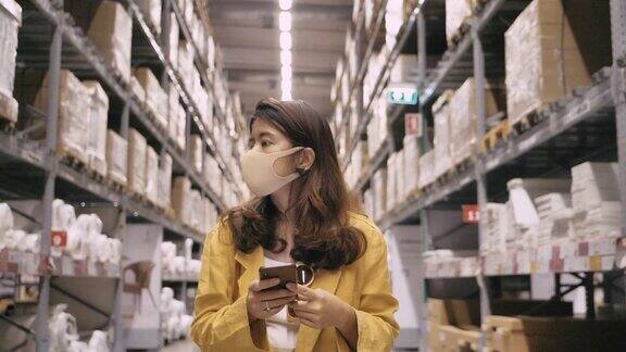 在仓库里戴着口罩使用智能手机的女人