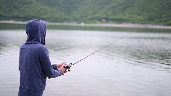 一个渔夫在一个天然的湖边钓鱼背景是山