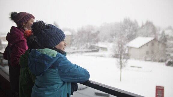 孩子们站在阳台上看雪