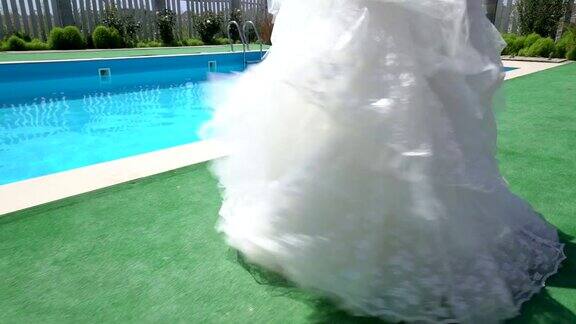 穿着白色婚纱的年轻女孩沿着室外游泳池散步