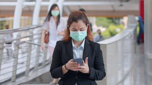 商业女性戴着保护面罩站在人群中使用智能手机慢镜头