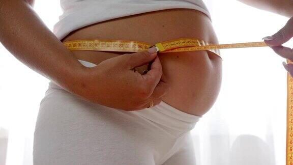 怀孕女性拿着卷尺的特写在白色背景下的大肚子