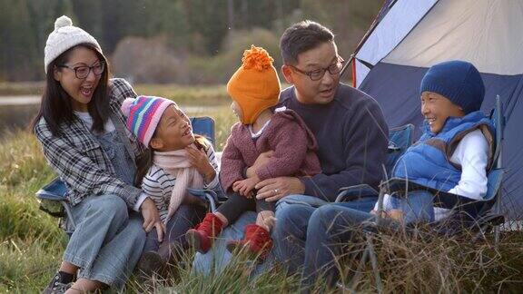 一个亚洲家庭在露营旅行中在帐篷外交谈