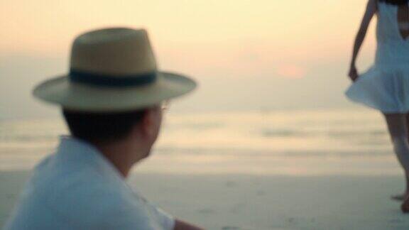 一名亚洲男子在沙滩上用手机拍摄了他的妻子在夏日日落时的照片