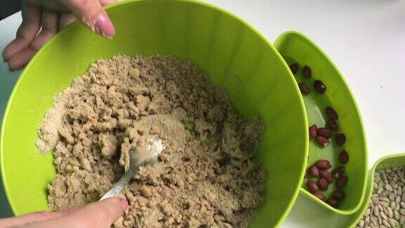 一名妇女在一个容器里用勺子混合蜂蜜和碾碎的花生和葵花籽混合它们来制作halva
