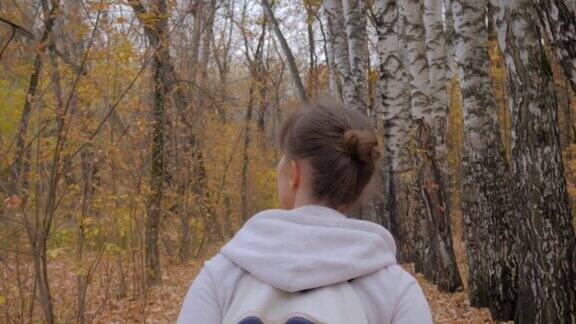年轻女子背着背包在秋天公园散步的后视图-摄影机镜头