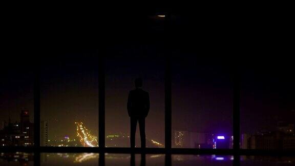 这名男子站在城市夜景的全景窗旁