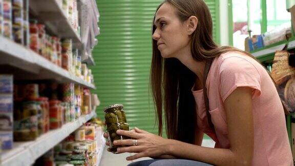 一名女子从超市货架上挑选罐装食品并阅读标签