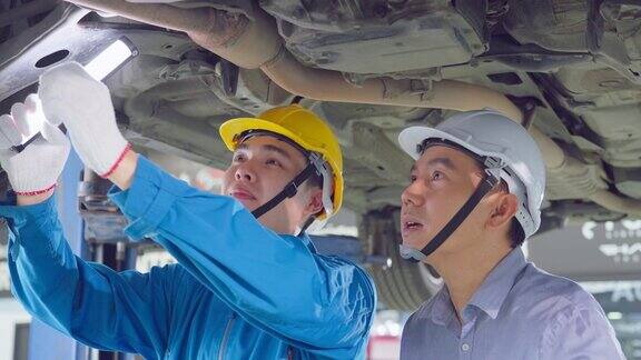 亚洲两名汽车机械师男子戴着头盔在机械厂工作车辆维修经理男工组在车况下检查维修车间的发动机