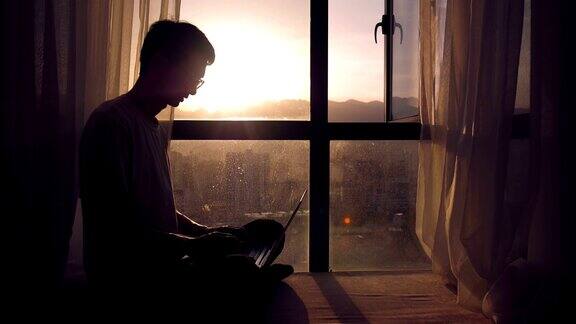 日落时分一个人坐在窗边用着笔记本电脑