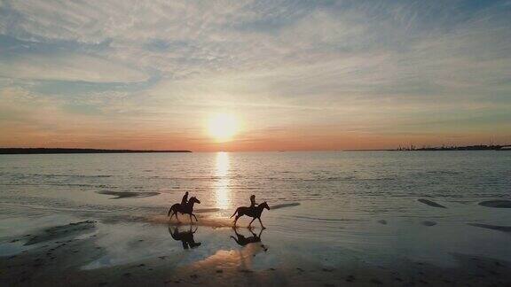 两个女孩在海滩上骑马马儿奔向大海在这张航拍照片中可以看到美丽的日落
