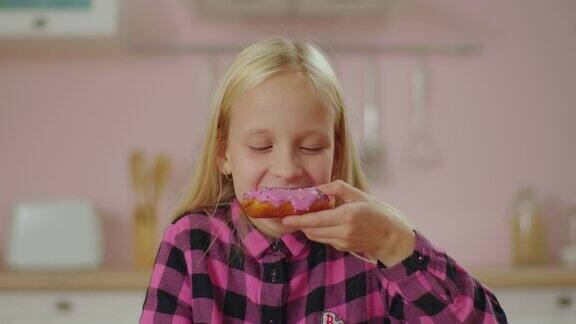 可爱的金发小女孩喜欢在粉红色的厨房吃粉红色的甜甜圈微笑的女孩子咬甜甜圈吃小孩的特写