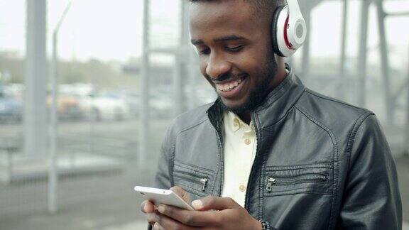 非裔美国潮人戴着耳机触摸外面的智能手机屏幕