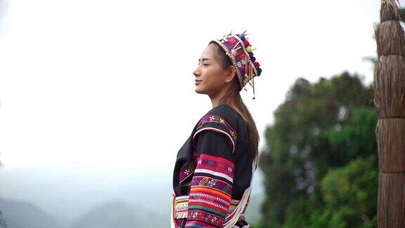 年轻的亚洲女性穿着传统服装站在一个木制平台上欣赏自然山景