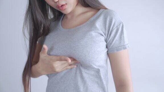 一名穿着灰色t恤的亚洲女性正在自我检查是否患有乳腺癌