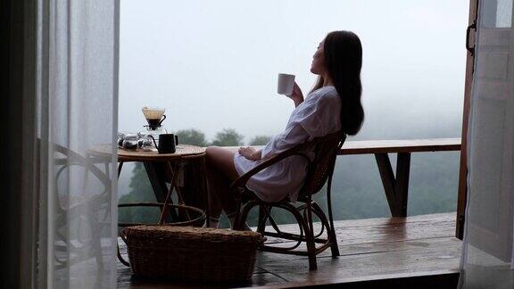 一个女人喝着滴滤咖啡在雾天欣赏美丽的自然风景
