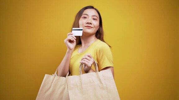 女人拿着购物袋和信用卡在孤立的黄色背景