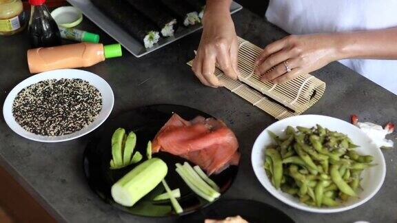 熟练的妇女用竹席卷起传统的寿司由黄瓜、鳄梨和烟熏鲑鱼制成