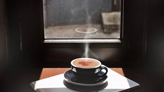 一杯冒着蒸汽的卡布奇诺咖啡静静地躺在一扇窗户前有淡淡的光线透进来