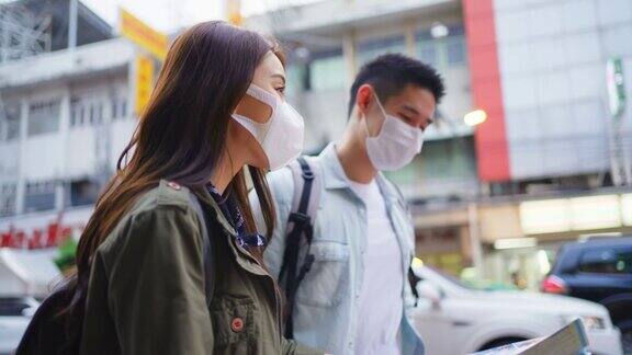 亚洲浪漫情侣戴口罩在城市旅行度蜜月新婚男女背包客看手机寻找目的地在疫情期间一起享受假期
