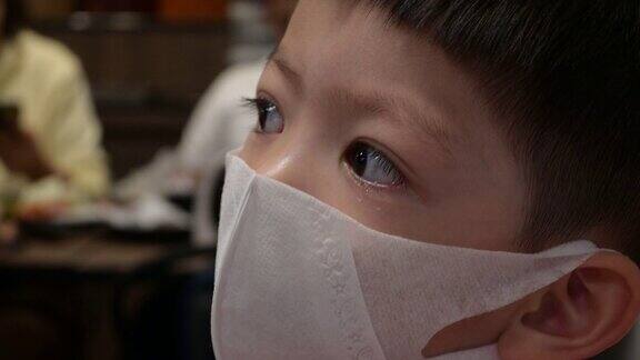 亚洲小男孩戴上卫生防护口罩在餐厅预防冠状病毒COVID-19大流行