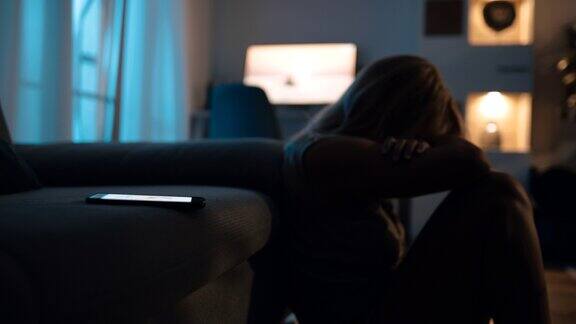 抑郁的女人晚上坐在地板上手机放在沙发上