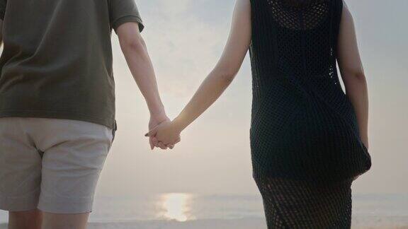 日出时幸福的情侣牵着手在海滩上散步