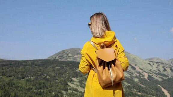 穿着黄色雨衣徒步旅行的年轻女子站在山上