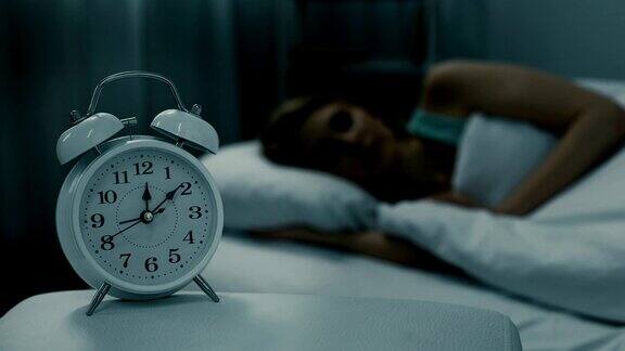 女人睡在闹钟显示午夜时间的床上晚上做梦