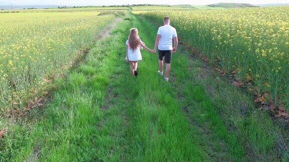 孩子们:兄弟姐妹走在长满草的小路上周围是长满油菜花的田野