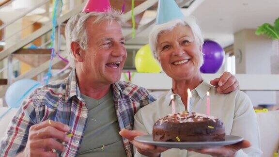 戴着派对帽的白人老夫妇用蛋糕和金色纸屑进行生日视频通话