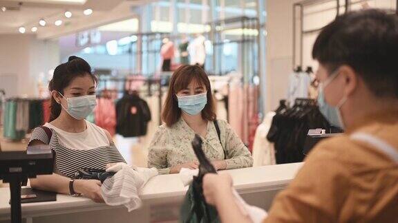亚洲华人服饰店收银员在柜台接受带口罩的顾客的信用卡