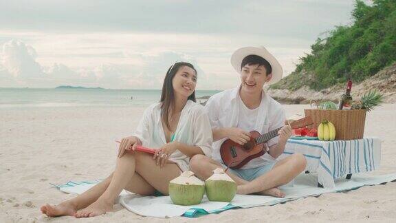 亚洲情侣在海滩上弹奏四弦琴一起唱歌享受情侣蜜月之旅夏季、假期、假期和快乐的泰国人概念