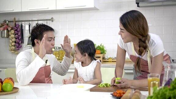 4k慢镜头年轻的亚洲父亲母亲和女儿快乐和乐趣准备蔬菜和果汁在一个现代化的白色厨房女儿做饭时心情愉快