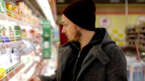 年轻男子推着购物车在超市的冰箱里买东西