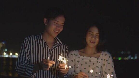 这对幸福的夫妇在晚上的焰火节上手持花灯欣赏烟花表演