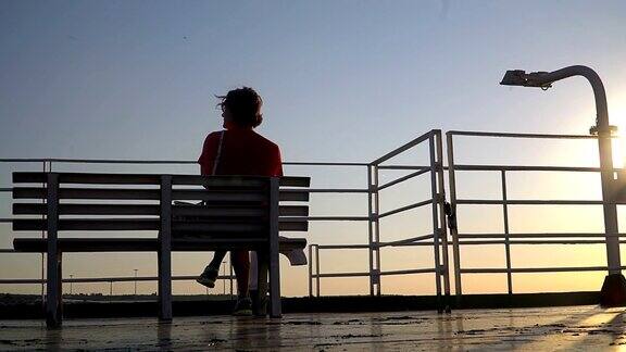 日落时分一位年长妇女坐在游艇甲板上的剪影