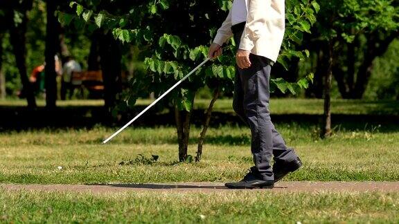 一名视力受损的男子拄着拐杖在公园的小路上摸索着前进