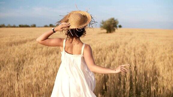 一个美丽的女孩穿着白色的夏装戴着草帽在麦田里自由奔跑背后的观点