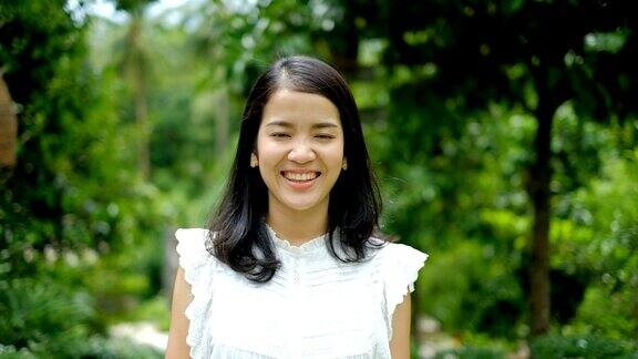 快乐年轻的亚洲妇女在白色西装微笑和笑对绿色的自然背景
