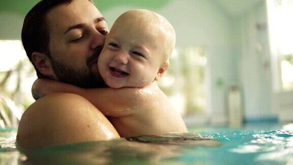 可爱的小婴儿和他的爸爸在游泳池里上游泳课父亲把儿子抱在手里拥抱着他小男孩开心地笑着