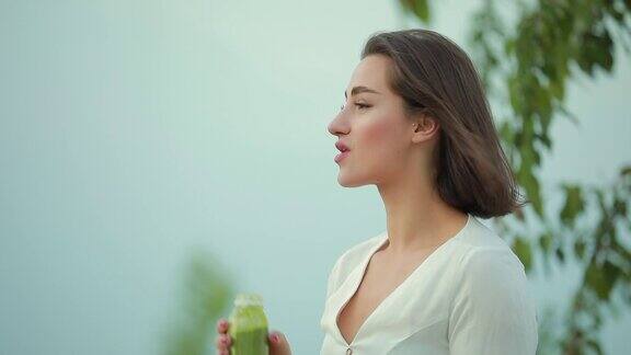 美丽的女人在户外喝绿色冰沙
