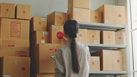 亚洲妇女在网上商店仓库检查库存库存货架上的包裹盒子网上电子商务零售的小商业概念