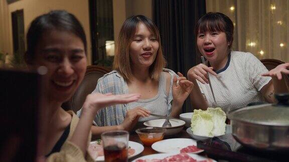 一群快乐的亚洲朋友一边吃火锅一边自拍视频通话晚上在家里聚在一起吃春节团圆饭生活方式享受美食