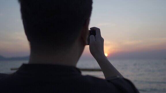 亚洲男人拿着手机在海滩与日落