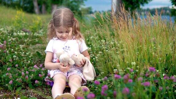 一个小女孩在盛开的三叶草中间的草地上玩玩具兔子